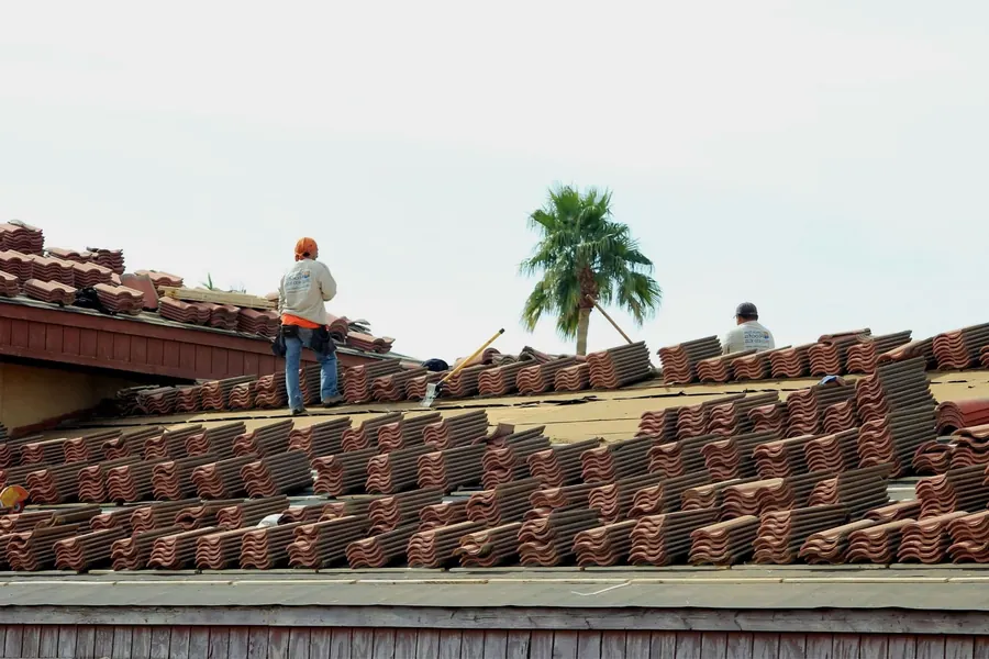 Roofers laying terra cotta tiles on a roof under a sunny sky with a palm tree behind