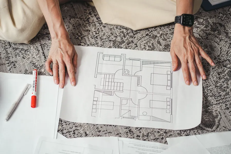 Hands smoothing out a printed floor plan on the floor next to a red marker